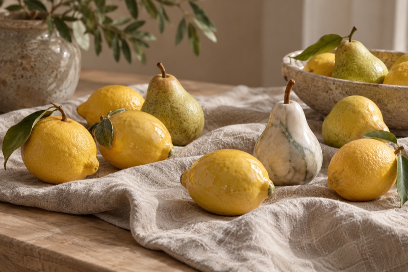 Glazed ceramic lemons and a marble pear mingle with real lemons and pears on rumpled linen.